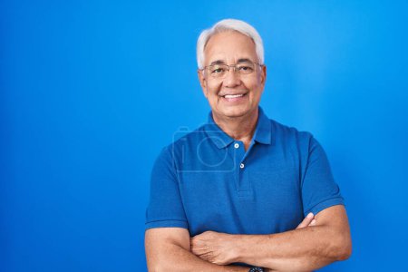 Téléchargez les photos : Middle age man with grey hair standing over blue background happy face smiling with crossed arms looking at the camera. positive person. - en image libre de droit