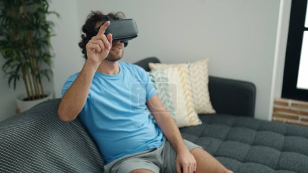 Foto de Joven hispano jugando videojuegos usando gafas de realidad virtual en casa - Imagen libre de derechos