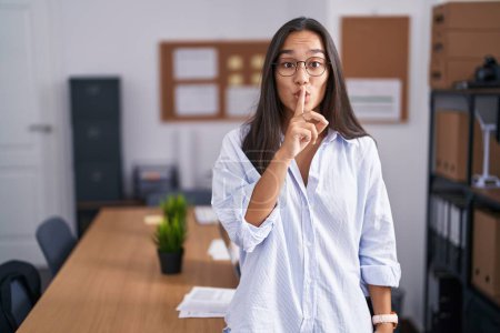 Téléchargez les photos : Young hispanic woman at the office asking to be quiet with finger on lips. silence and secret concept. - en image libre de droit