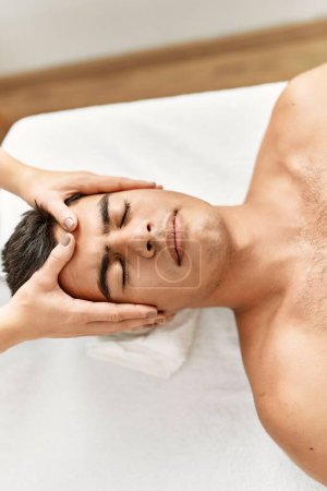 Photo for Young hispanic man relaxed having facial massage at beauty center - Royalty Free Image