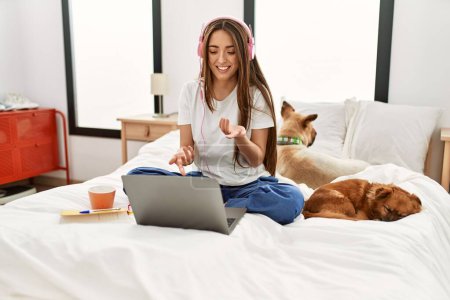 Téléchargez les photos : Jeune femme hispanique ayant appel vidéo assis sur le lit avec des chiens dans la chambre - en image libre de droit