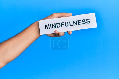 Hand of caucasian man holding paper with mindfulness word over isolated blue background