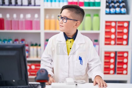 Foto de Young hispanic kid working at pharmacy drugstore looking to side, relax profile pose with natural face and confident smile. - Imagen libre de derechos