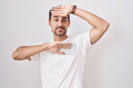Foto de Handsome hispanic man standing over white background smiling cheerful playing peek a boo with hands showing face. surprised and exited - Imagen libre de derechos