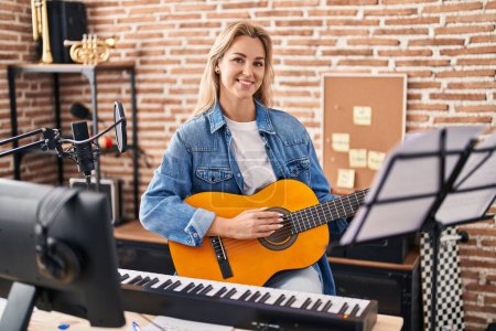 Photo for Young blonde woman musician singing song playing spanish guitar at music studio - Royalty Free Image