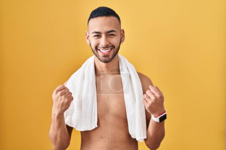 Photo for Young hispanic man standing shirtless with towel very happy and excited doing winner gesture with arms raised, smiling and screaming for success. celebration concept. - Royalty Free Image