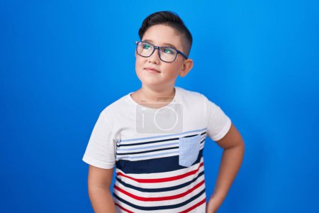 Photo for Young hispanic kid standing over blue background smiling looking to the side and staring away thinking. - Royalty Free Image