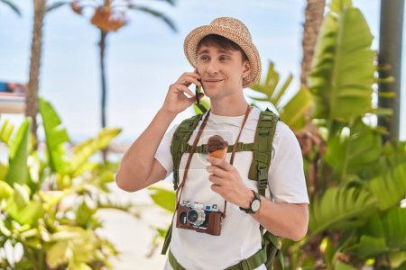 Foto de Joven hombre caucásico turista hablando en smartphone comiendo helado en el parque - Imagen libre de derechos