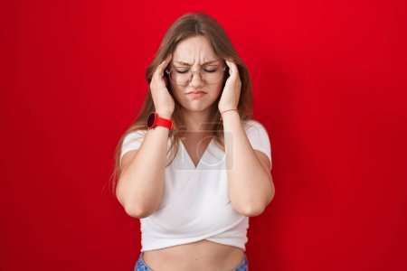 Téléchargez les photos : Jeune femme caucasienne debout sur fond rouge avec la main sur la tête, maux de tête parce que le stress. migraine souffrant. - en image libre de droit