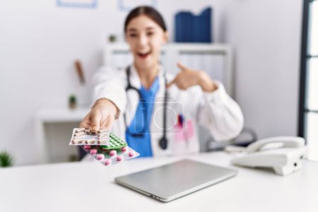 Photo for Young hispanic doctor woman wearing doctor uniform holding prescription pills at clinic pointing finger to one self smiling happy and proud - Royalty Free Image