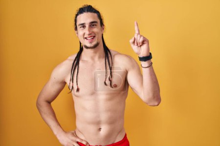 Photo for Hispanic man with long hair standing shirtless over yellow background pointing finger up with successful idea. exited and happy. number one. - Royalty Free Image