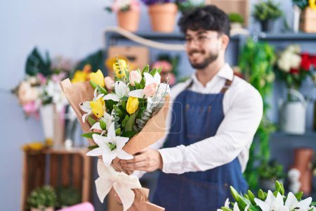 Téléchargez les photos : Young hispanic man florist holding bouquet of flowers at florist shop - en image libre de droit