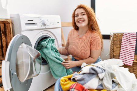 Foto de Joven pelirroja limpiando ropa usando lavadora en la lavandería - Imagen libre de derechos