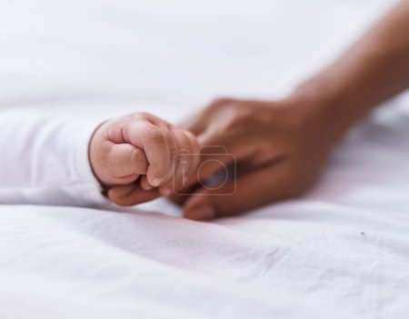 Téléchargez les photos : Adorable bambin hispanique couché sur le lit tenant doigt mère dans la chambre - en image libre de droit