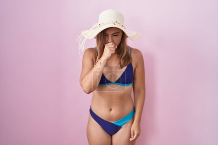 Téléchargez les photos : Jeune femme hispanique portant un bikini sur fond rose se sentant mal à l'aise et toussant comme symptôme de rhume ou de bronchite. concept de soins de santé. - en image libre de droit