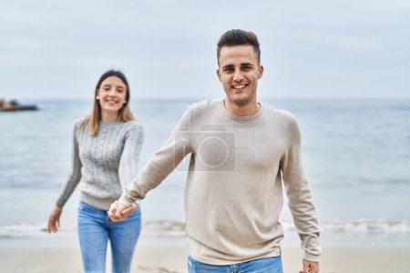 Téléchargez les photos : Homme et femme couple souriant confiant marche avec les mains ensemble au bord de la mer - en image libre de droit