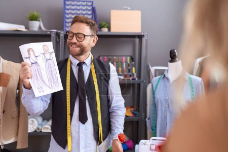 Photo for Middle age man tailor showing clothing design to client at atelier - Royalty Free Image