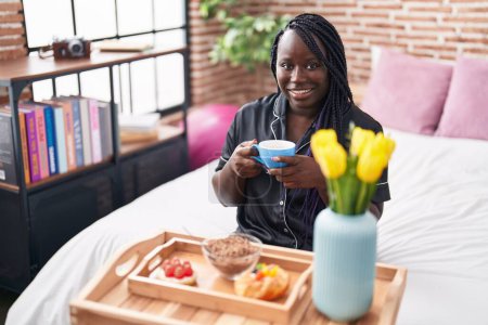 Photo for African american woman having gift breakfast sitting on bed at bedroom - Royalty Free Image