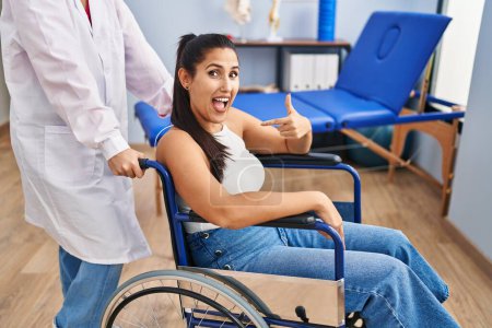 Photo for Young hispanic woman sitting on wheelchair at physiotherapy clinic pointing finger to one self smiling happy and proud - Royalty Free Image