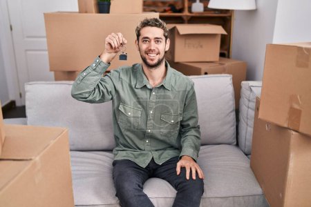 Photo for Hispanic man with beard holding keys of new home looking positive and happy standing and smiling with a confident smile showing teeth - Royalty Free Image