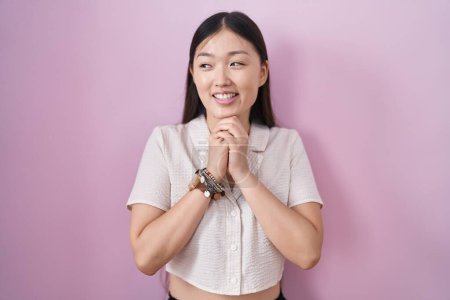 Photo for Chinese young woman standing over pink background laughing nervous and excited with hands on chin looking to the side - Royalty Free Image