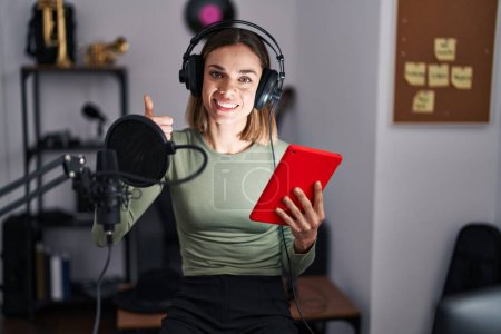 Téléchargez les photos : Hispanic woman singing song using microphone and tablet smiling happy and positive, thumb up doing excellent and approval sign - en image libre de droit
