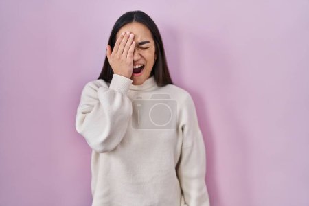 Foto de Young south asian woman standing over pink background yawning tired covering half face, eye and mouth with hand. face hurts in pain. - Imagen libre de derechos