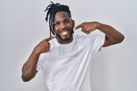 Photo for African man with dreadlocks wearing casual t shirt over white background smiling cheerful showing and pointing with fingers teeth and mouth. dental health concept. - Royalty Free Image