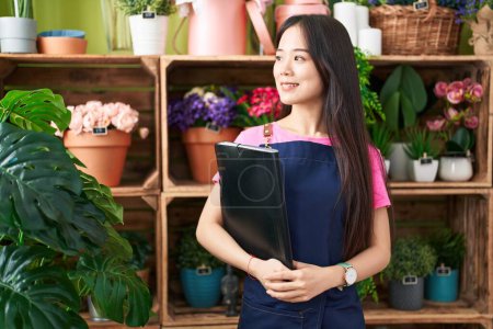 Photo for Young chinese woman florist smiling confident holding binder at flower shop - Royalty Free Image