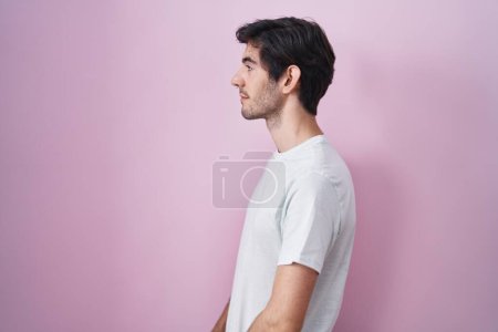 Téléchargez les photos : Jeune homme hispanique debout sur fond rose regardant vers le côté, pose de profil relax avec visage naturel et sourire confiant. - en image libre de droit