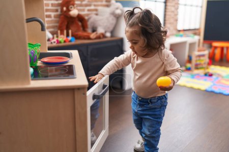 Photo for Adorable hispanic girl playing with play kitchen standing at kindergarten - Royalty Free Image