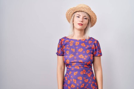 Photo for Young caucasian woman wearing flowers dress and summer hat relaxed with serious expression on face. simple and natural looking at the camera. - Royalty Free Image