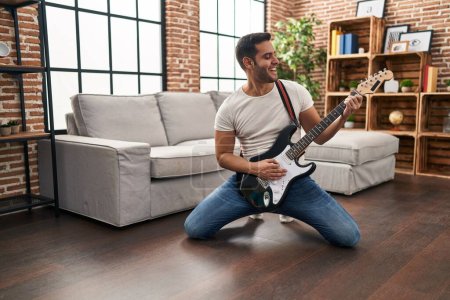 Photo for Young hispanic man playing electrical guitar with knees on floor at home - Royalty Free Image