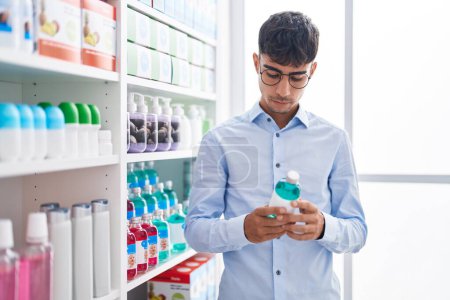 Téléchargez les photos : Jeune homme hispanique client lecture bouteille de médicaments étiquette à la rue - en image libre de droit