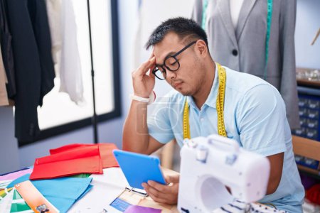 Téléchargez les photos : Young chinese man tailor using touchpad with serious expression at tailor shop - en image libre de droit