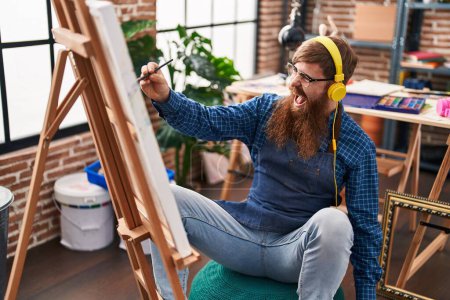 Téléchargez les photos : Young redhead man artist listening to music drawing at art studio - en image libre de droit