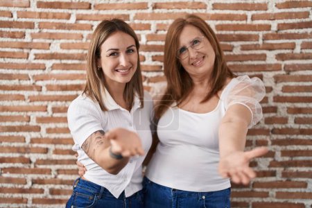 Photo for Hispanic mother and daughter wearing casual white t shirt smiling cheerful offering palm hand giving assistance and acceptance. - Royalty Free Image