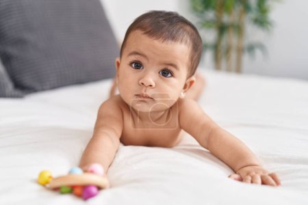 Téléchargez les photos : Adorable hispanic baby lying on bed holding rattle at bedroom - en image libre de droit