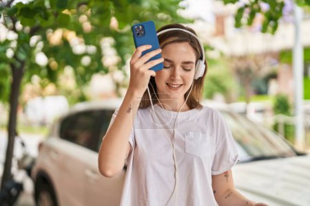Téléchargez les photos : Jeune femme souriante à l'écoute de la musique dans la rue - en image libre de droit