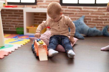 Foto de Adorable toddler playing with car toy sitting on floor at kindergarten - Imagen libre de derechos