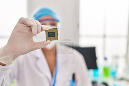 Foto de Mujer de mediana edad que usa unifor científico y máscara médica que sostiene el procesador de CPU en el laboratorio - Imagen libre de derechos