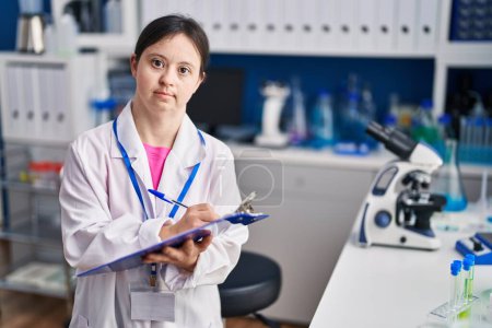 Photo for Young woman with down syndrome scientist writing on clipboard at laboratory - Royalty Free Image