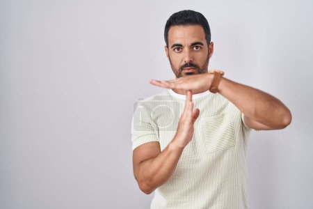 Foto de Hispanic man with beard standing over isolated background doing time out gesture with hands, frustrated and serious face - Imagen libre de derechos