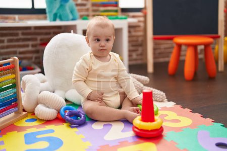 Téléchargez les photos : Adorable bébé caucasien jouant avec des cerceaux jouet assis sur le sol à la maternelle - en image libre de droit