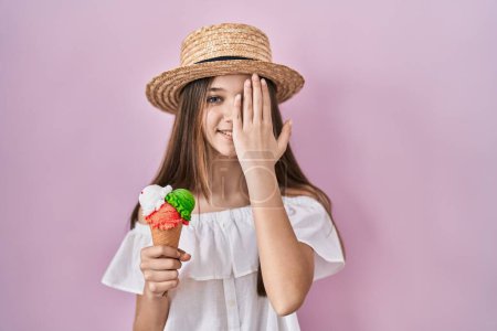 Téléchargez les photos : Teenager girl holding ice cream covering one eye with hand, confident smile on face and surprise emotion. - en image libre de droit