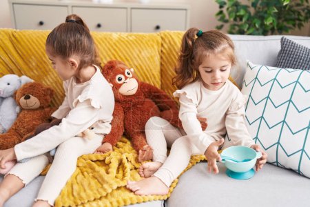 Photo for Two kids playing with dolls sitting on sofa at home - Royalty Free Image