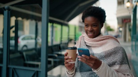 Téléchargez les photos : Jeune femme afro-américaine utilisant un smartphone buvant du café dans la rue - en image libre de droit