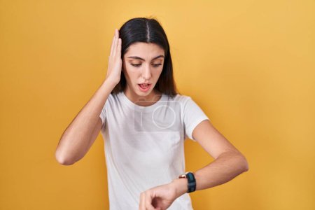 Téléchargez les photos : Young beautiful woman standing over yellow background looking at the watch time worried, afraid of getting late - en image libre de droit