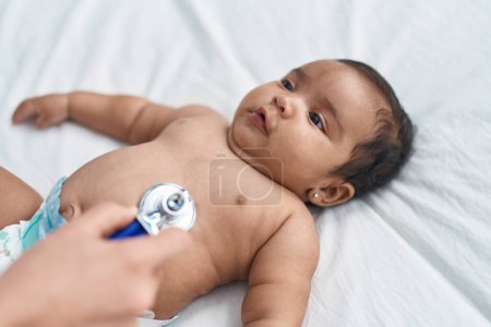 Téléchargez les photos : Bébé afro-américain ayant un examen médical couché sur le lit dans la chambre - en image libre de droit