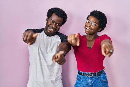 Téléchargez les photos : Jeune couple afro-américain debout sur fond rose pointant vers vous et la caméra avec les doigts, souriant positif et joyeux - en image libre de droit